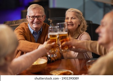 Portrait of smiling senior people drinking beer in bar and clinking glasses while enjoying night out with friends - Powered by Shutterstock