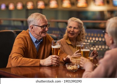 Portrait of smiling senior people drinking beer in bar while enjoying night out with friends, copy space