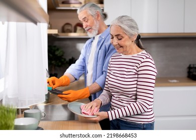 Portrait Of Smiling Senior Spouses Washing Dishes Together In Kitchen After Lunch, Happy Married Elderly Couple Cleaning Plates And Chatting, Sharing Domestic Chores Together, Copy Space