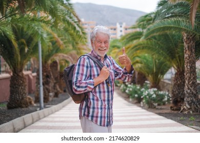 Portrait Of Smiling Senior Tourist Male With A Backpack And Thumb Up Walking Down The Street In Tenerife Enjoying Travel And Holiday