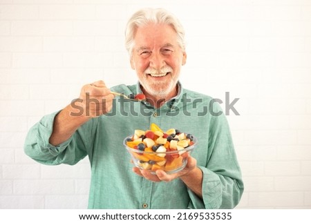 Portrait of smiling senior white-haired man ready to eat a salad of fresh summer fruits. Breakfast or lunch time, healthy eating