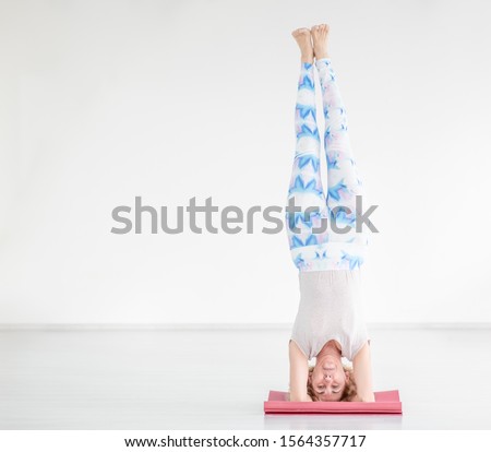 Portrait of a smiling senior woman doing advanced yoga or pilates. Supported headstand, salamba sirsasana. Empty space for text