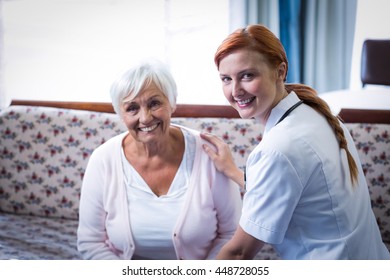 Portrait of smiling senior woman and female doctor in living room at home