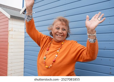 Portrait of smiling senior woman with hands raised against blue hut - Powered by Shutterstock