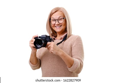 Portrait Of Smiling Senior Woman Photographer 60-65 Years Old With Blonde Hair Standing, Holding Photocamera In Hands And Looking At Camera. Concept Of Lifestyle. Isolated On White. 