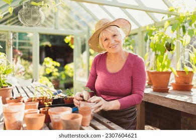 Portrait smiling senior woman potting plants in greenhouse - Powered by Shutterstock