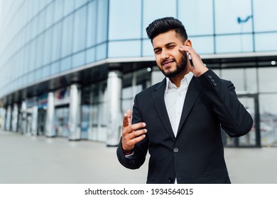 Portrait Of A Smiling Serious Indian Man Talking On Wireless Headphones And Gesturing To The Camera, Place For Text.