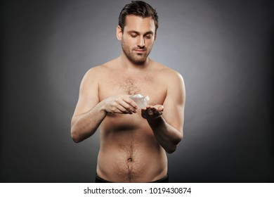 Portrait Of A Smiling Shirtless Man Using Aftershave Lotion Isolated Over Gray Background