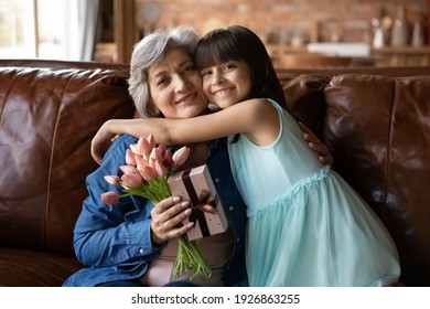 Portrait Of Smiling Small Girl Child Hug Congratulate With Mother Day Excited Senior Grandmother. Happy Cute Little 8s Kid Greeting Mature Grandparent, Present Flowers And Gift. Anniversary Concept.