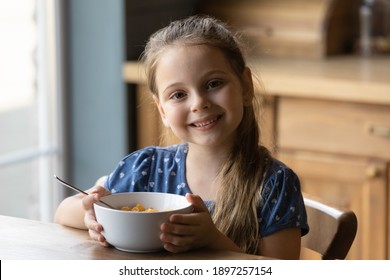 Portrait Of Smiling Small Girl Sit At Desk At Home Kitchen Have Delicious Tasty Nutritious Breakfast. Happy Little Child Eat Healthy Cereals With Wholegrain Milk In Kitchen. Children Nutrition Concept