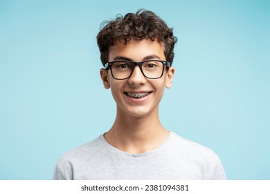 Portrait of smiling smart school boy with braces wearing glasses isolated on blue background. Education concept - Powered by Shutterstock