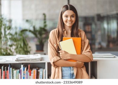 Portrait of smiling smart teenage girl holding book looking at camera standing in modern classroom, copy space. Back to school, education concept - Powered by Shutterstock