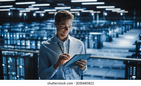 Portrait Of Smiling IT Specialist Using Tablet Computer In Data Center. Big Server Farm Cloud Computing Facility With Male Maintenance Administrator Working. Cyber Security, E-Business.