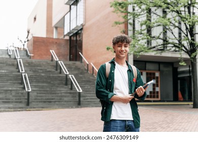 Portrait of smiling student guy standing on university campus building. Happy looking at the camera ready for lecture - Powered by Shutterstock