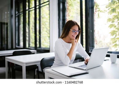 Portrait of smiling student looking at laptop in modern study room.