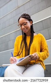 Portrait Of Smiling Student Sitting Outside Taking Notes In Her Notebook