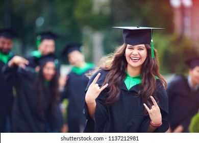 portrait of smiling successful indian student in graduation gown with rock n roll hand gesture