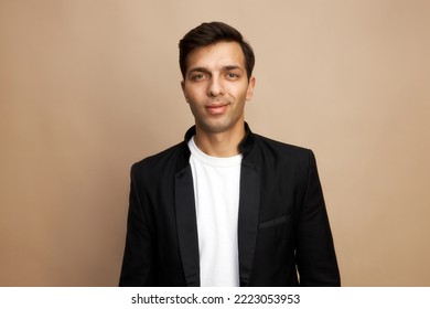 Portrait Of Smiling Successful Young Handsome Businessman Participating In Tender Process, Isolated On Brown Studio Background In White T-shirt And Black Jacket, Feeling Himself Confident