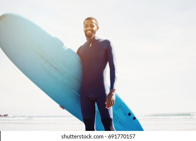 Portrait Of Smiling  Surfer Man With Surf Board On The Beach. Mixed Race Black Skin And Beard. Summer Sport Activity 