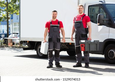 Portrait Of A Smiling Technicians Standing Against The Truck Holding Tool Box In Hands