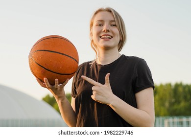 Portrait of smiling teen girl basketball player pointing with finger to ball - Powered by Shutterstock