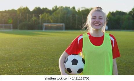 Portrait of a smiling teen girl football player with a soccer ball at sunset, copyspace