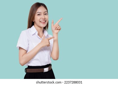 Portrait smiling of teen student girl of Asian ethnicity in university uniform pointing finger away on copy space isolated on light blue color background. - Shutterstock ID 2237288031