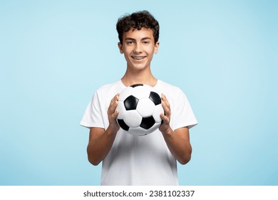 Portrait of smiling teenage boy holding ball playing football isolated on blue background. Sport, hobby, competition concept  - Powered by Shutterstock