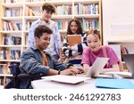 Portrait of smiling teenage boy using laptop in school library with diverse group of students working on project together