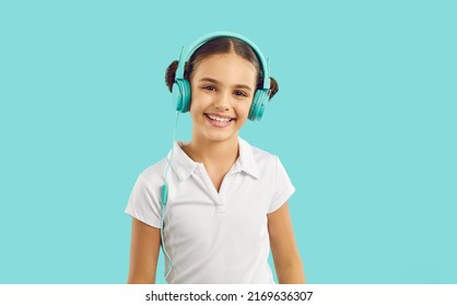 Portrait Of Smiling Teenage Girl Child In Headphones Isolated On Blue Studio Background Listen To Music. Happy Funny Teen Kid Enjoy Good Quality Sound In Modern Earphones. Hobby And Entertainment.