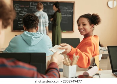 Portrait of smiling teenage schoolgirl handing note to friend in class - Powered by Shutterstock