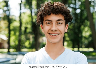 Portrait of smiling teenager boy with braces looking at camera posing in the park. Lifestyle emotions concept - Powered by Shutterstock