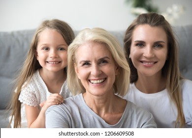 Portrait of smiling three generations of women look at camera posing for family picture at home, happy mother, daughter and grandmother in the middle embrace together showing love and support