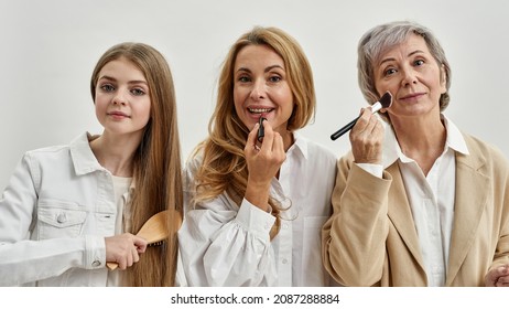 Portrait of smiling three generations of women isolated on white studio background do makeup together. Happy teen girl child with young mother and elderly grandmother beauty routine procedures.