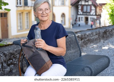 Portrait of smiling traveler senior woman sitting on a bench visiting an old swiss village - holidays travel concept - Powered by Shutterstock