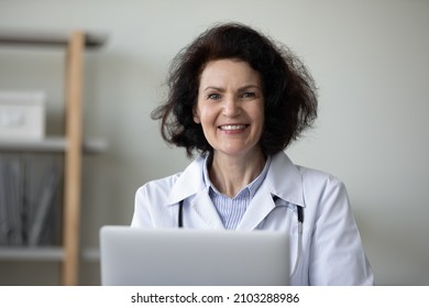 Portrait of smiling trusted older senior 60s female general practitioner doctor physician sitting at table with computer, working in clinic office. healthcare medical service, telemedicine concept.