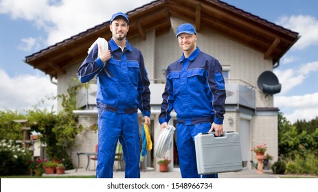 Portrait Of Smiling Two Young Male Electrician Standing In Front Of House With Electrician Kits - Powered by Shutterstock