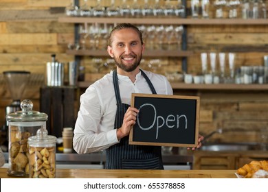 Portrait of smiling waiter standing with open sign board in cafe - Powered by Shutterstock