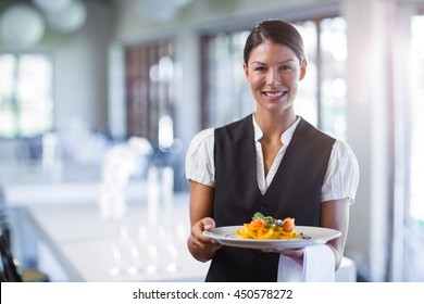 Portrait of smiling waitress holding plate of meal in a restaurant