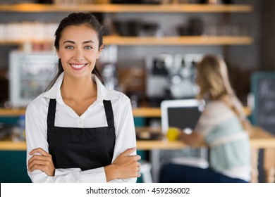 Portrait of smiling waitress standing with arms crossed in cafe