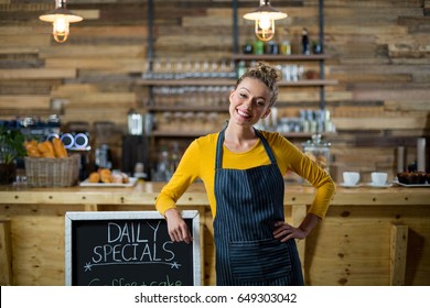 Portrait of smiling waitress standing with menu board in cafe - Powered by Shutterstock