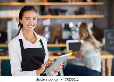 Portrait of smiling waitress using digital tablet in cafe