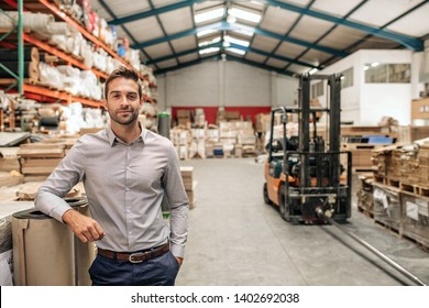 Portrait of a smiling warehouse manager leaning against some stock with piles of carpets on shelves and a forklift in the background - Powered by Shutterstock