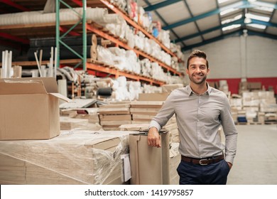 Portrait of a smiling warehouse manager leaning against some stock with piles of carpets stacked on shelves in the background