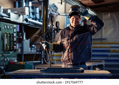 Portrait of a smiling welder posing at his workplace in the factory, and it is obvious that the master is engaged in welding.