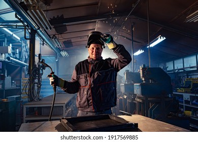 Portrait of a smiling welder posing at his workplace in the factory, and it is obvious that the master is engaged in welding.