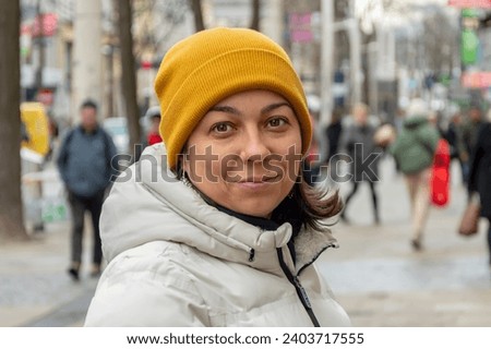 Portrait of a smiling woman 40-45 years old in a hat on a blurred background of a street of a European city and people passing by.