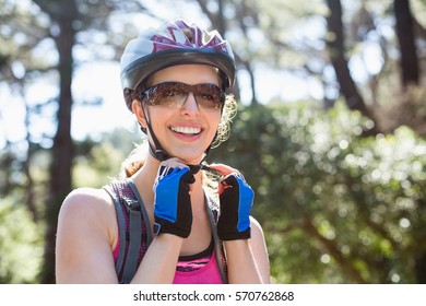 Portrait of smiling woman adjusting helmet against tree at forest - Powered by Shutterstock