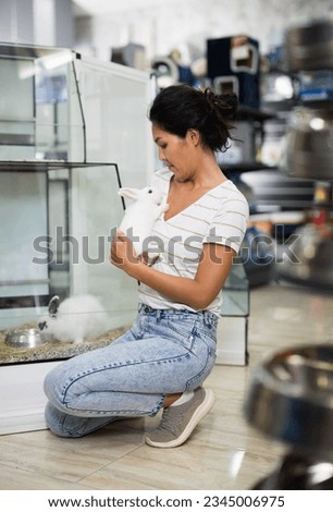 Portrait of smiling woman choosing new pet in store, holding cute rabbit