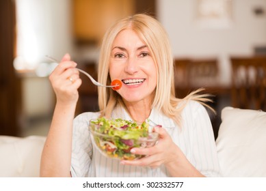 Portrait of a smiling woman eating an healthy salad in her living room - Powered by Shutterstock